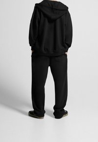 Felpa nera con cappuccio e pantaloni della tuta coordinati, realizzati in tessuto morbido, con cappuccio, vestibilità rilassata e tasche in un design senza cuciture.