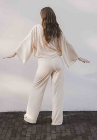Crème-kleurige loungewear-set met brede mouwen en een elastische tailleband, gemaakt van zacht materiaal en met een ontspannen pasvorm; gefotografeerd van achter.