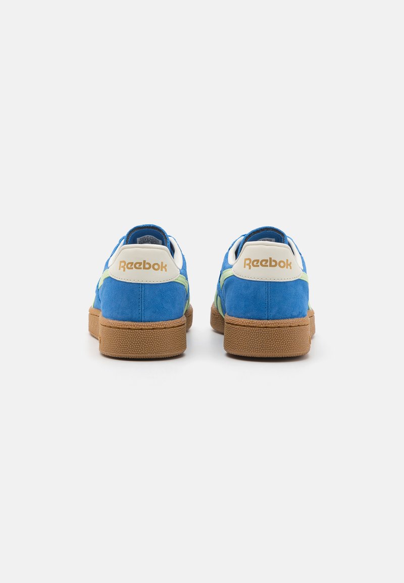 Blaue Wildledersneaker mit grünen Akzenten und einer braunen Gummisohle. Verfügt über eine weiße Fersenschlaufe mit goldenem "Reebok"-Logo.