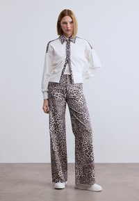 Λευκό πλεκτό σακάκι με λεπτομέρειες λεοπάρ, συνδυασμένο με παντελόνια με σχέδιο λεοπάρ σε αποχρώσεις του γκρι και καφέ, ολοκληρωμένο με λευκά αθλητικά παπούτσια.