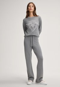 Grijs gebreide loungewear set met een loose-fit sweatshirt met een logo en broek met elastische taille, in combinatie met witte sneakers.