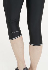 Svarta capri leggings i mjukt material, med en silverdetalj vid fållen och "ENDURANCE"-logotypen i vitt på vaden.