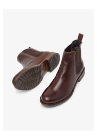 Botas Chelsea de cuero marrón con paneles laterales elásticos, suelas texturizadas y lengüetas. Presentan un diseño elegante y detalles de costura.
