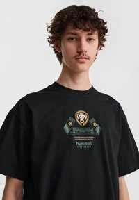 Czarna bawełniana koszulka z grafiką w zielonych i złotych akcentach, z logo "SWARM International" oraz marką "hummel".