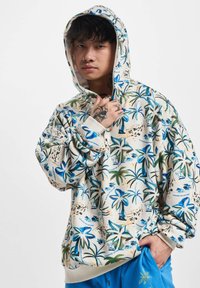Sudadera con capucha de fondo crema, que presenta un estampado colorido de palmeras en azul y verde. Fabricada en tejido suave con puños y dobladillo acanalados.