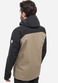 Veste imperméable avec une partie supérieure noire et une partie inférieure beige, dotée d'un col haut et d'un tissu texturé. Comprend un détail de logo sur la manche.