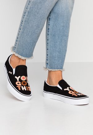 Person wearing light blue frayed hem jeans and black slip-on sneakers with white soles and "YOU GOT THIS" text on top.