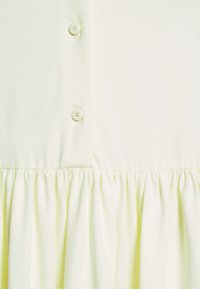 Gros plan sur un tissu jaune pâle avec deux boutons cousus et un détail de couture froncée sous les boutons.