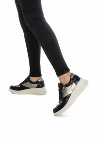 Baskets noires et métalliques avec une surface texturée, dotées d'une semelle blanche épaisse et d'un détail de zip latéral. Accents de motifs lisses et reptiles.