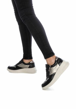 Zapatillas negras y plateadas con un acabado texturizado, que cuentan con un detalle de cremallera y una suela blanca gruesa. El material suave y brillante contrasta con el acabado mate.