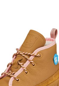 Brauner Lederstiefel mit strukturiertem Finish, pinken Schnürsenkeln und einer Gummisohle. Hat ein eingeprägtes Katzen Gesicht auf der Zunge und einen blauen Logoakzent.