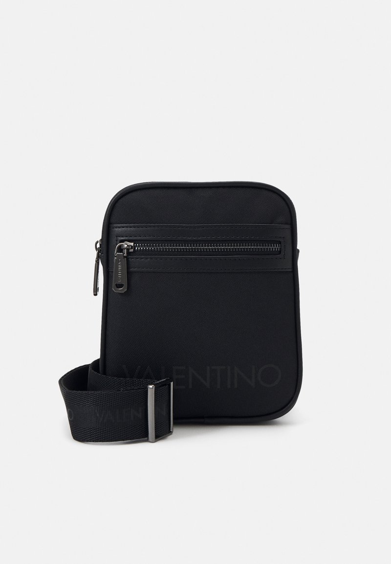 Černá nylonová crossbody taška s přední kapsou na zip, nastavitelným popruhem a minimalistickým designem. Hladká textura a obdélníkový tvar.