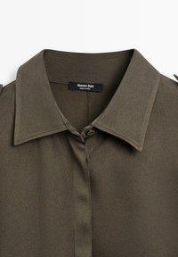Chemise vert olive avec un col structuré et une patte de boutonnage. Fabriquée en tissu lisse, avec une étiquette portant la mention "Massimo Dutti."