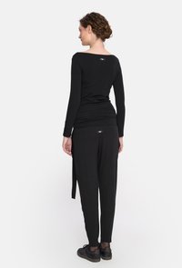 Czarna bluzka z długim rękawem o kroju off-shoulder, w połączeniu z czarnymi luźnymi spodniami. Materiał wydaje się miękki i ma gładkie wykończenie.