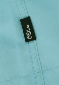 Lichtblauwe stof met een gladde textuur, met een zwart etiket met witte tekst dat "spitzbub studios" zegt, nabij een naad.