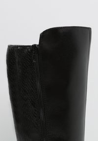 Bota negra hasta la rodilla con un acabado de estampado de serpiente texturizado en un lado y cuero liso en el otro, con un cierre de cremallera lateral.