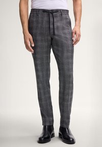 Pantalons à carreaux gris en tissu texturé, dotés d'une taille à cordon, d'une coupe slim et d'ourlets retournés. Portés avec des bottines noires.