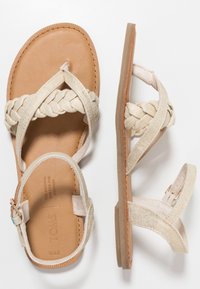 Vävd beige tygsandaler med en naturlig läderfotbädd och justerbar ankelsnor. Platt sula med texturerade kanter.