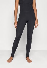 Μαύρες κολάν από ελαστικό ύφασμα, με ψηλή μέση και ανοίγματα στους αστραγάλους. Λείος υφιστάμενος χωρίς καθόλου εμφανείς σχέδια.