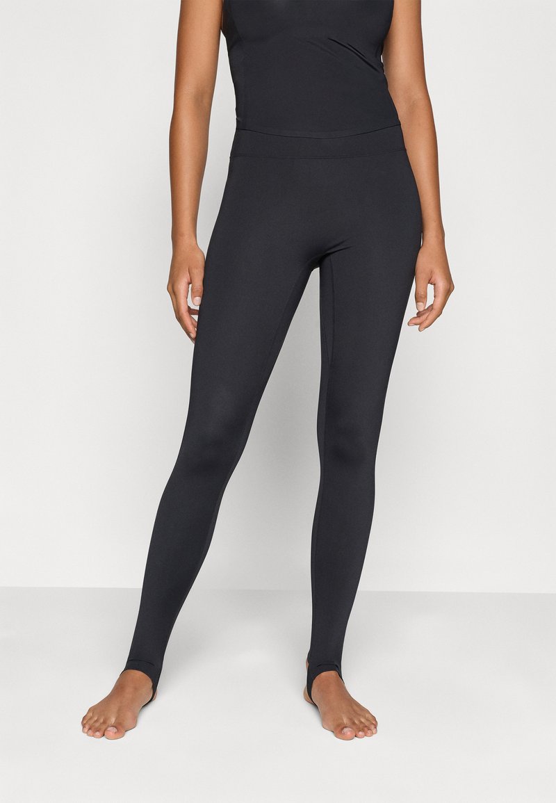 Μαύρες κολάν από ελαστικό ύφασμα, με ψηλή μέση και ανοίγματα στους αστραγάλους. Λείος υφιστάμενος χωρίς καθόλου εμφανείς σχέδια.