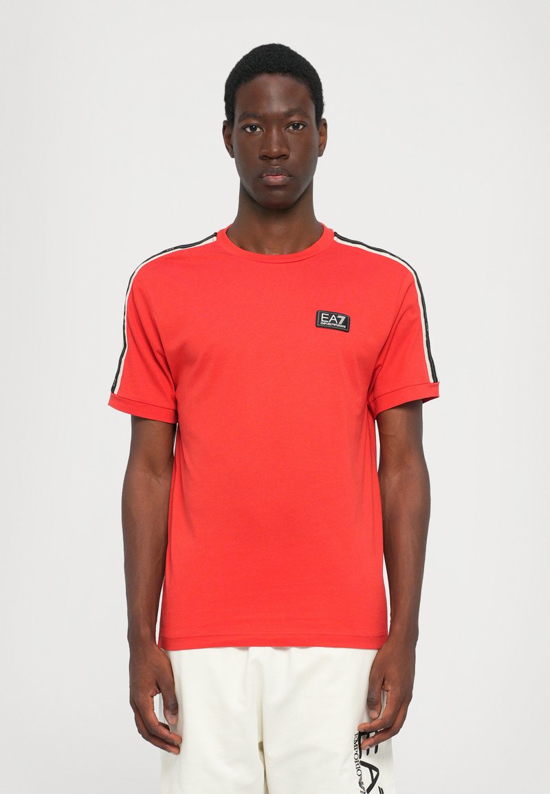 Red cotton t-shirt featuring a crew neck, short sleeves, and black side stripes. Includes an EA7 logo patch on the chest.