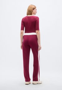 Μπορντό φόρμα με εφαρμοστή μπλούζα και χαλαρή παντελόνα. Λευκή ζώνη μέσης και πλευρικές ρίγες. Μαλακό ύφασμα και μίνιμαλ σχεδιασμός.