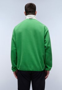 Green fleece pullover with a high collar. Features include a contrasting white collar and a sleek, relaxed fit design. Soft texture.