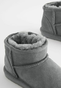 Graue Wildleder-Stiefeletten mit weicher, plüschiger Innenausstattung. Ausgestattet mit gesteppten Nähten, abgerundetem Oberrand und einer flachen Gummisohle.