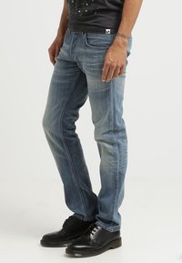 Jeans de denim azul claro con un corte ajustado, textura desgastada, costuras contrastantes y diseño de cinco bolsillos, combinados con zapatos negros.