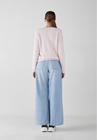 Pull en peluche rose clair, jeans en denim bleu clair ample, et baskets noir et blanc, vu de dos. Design minimaliste.