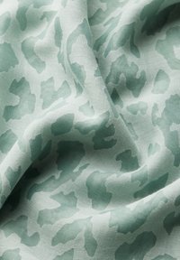 Lichtgroene stof met een subtiel dierenprintpatroon. De textuur lijkt soepel, met variërende tinten groen die door elkaar zijn geweven.