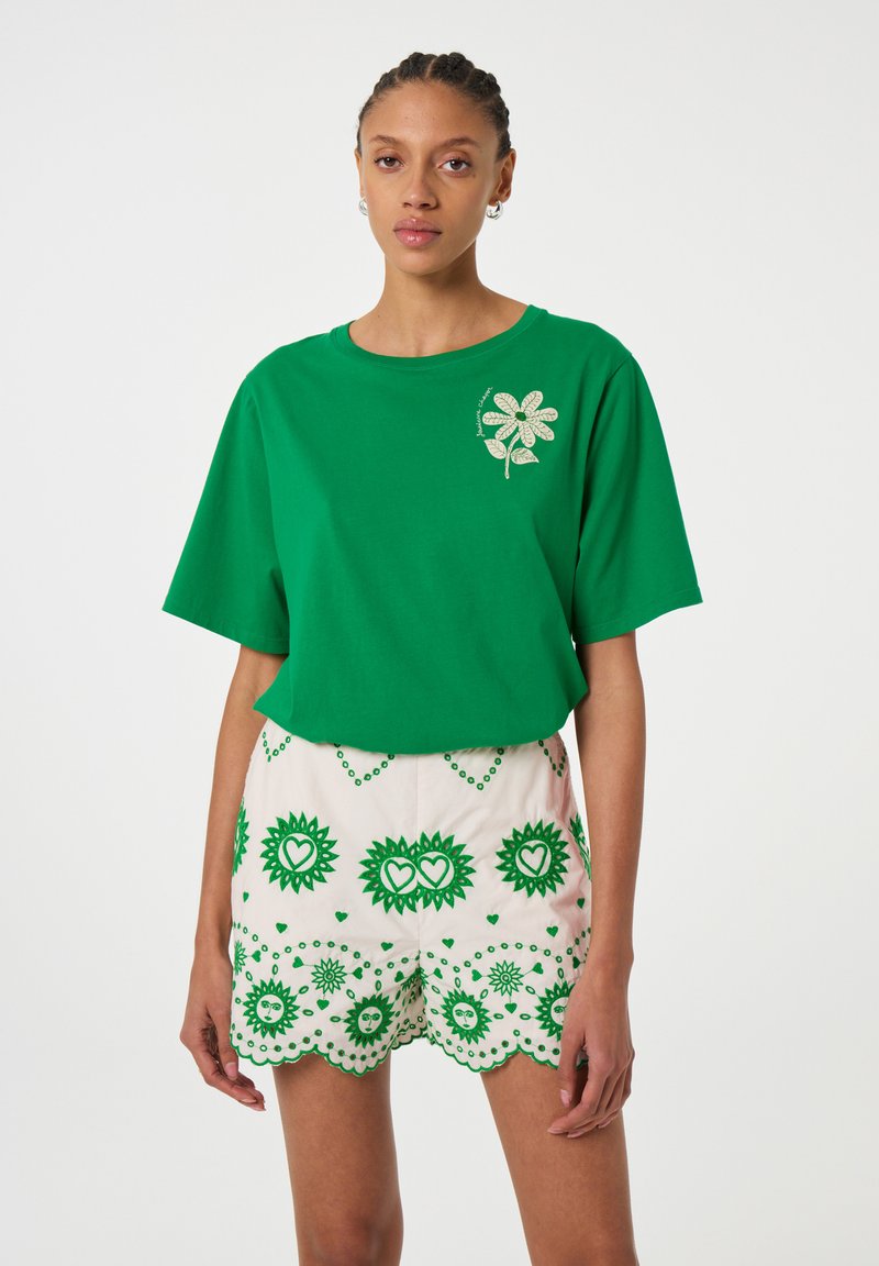 Groene katoen T-shirt met korte mouwen en bloemenborduurwerk aan de linkerkant, gecombineerd met crèmekleurige shorts met groene bloemen- en hartpatronen.