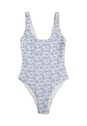 Femme portant des lunettes de soleil sombres et un maillot de bain blanc avec des motifs de coquillages bleus, allongée sur une serviette rouge à rayures blanches.