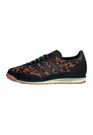 Laag uitgesneden Adidas sneaker met luipaardprint stof, zwarte suède overlays, groene veters en een gumzool met witte en groene middenzool accenten.