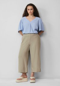 Lichtblauw V-hals blouse met korte pofmouwen, gecombineerd met beige wijde broekspijpen. Witte plateau-sandalen maken de outfit af.