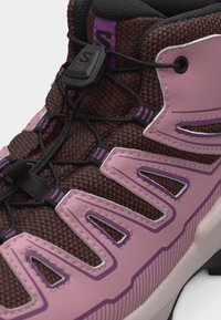 Lähivõte pruunist ja roosast matkasaapast, millel on mustad elastsed paelad ja plastmassist lukustus padi keeletüki peal.