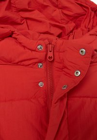 Giacca a vento rossa con chiusura a zip intera, bottoni a pressione e texture trapuntata. Il tessuto ha una finitura liscia con un leggero lucido.