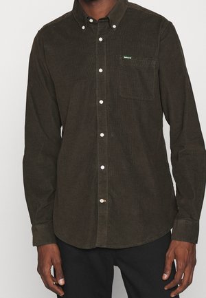 Donkergroene corduroy blouse met borstzak en witte knopen gedragen door een persoon met een donkere broek, armen ontspannen langs het lichaam.