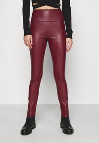 Burgundy faux läderleggings med hög midja, slät yta och slim fit, kombinerade med svarta ankelstövlar.