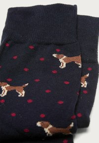 Calzini blu marino con motivi di cani marroni e pois rossi. Realizzati in materiale morbido con una texture a coste intorno ai polsini.