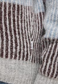 Il maglione in maglia presenta righe alternate in grigio e bordeaux, realizzato in un materiale morbido con una finitura testurizzata. Etichetta piccola visibile.