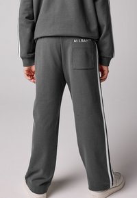 Sive bombažne trenirke z belimi stranskimi črtami, z zadnjim žepom in tiskanem logotipom. Mehka tekstura in ohlapen kroj.