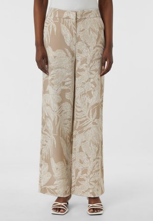 Beige wide-leg pants with abstract light beige leaf patterns worn with white strappy square-toe sandals and a white top.