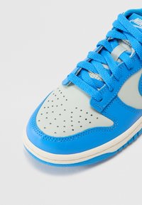 Blauer Leder-Sneaker mit grauem perforiertem Zehenbereich, blauen Schnürsenkeln und weißer Sohle. Verfügt über ein strukturiertes Design und genähte Akzente entlang der Kanten.