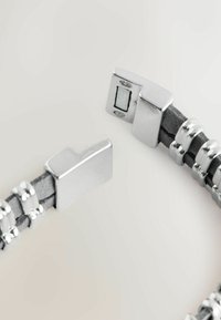 Grå læderarmbånd med sølvfarvede metal detaljer og en flad lukning, prydet med dekorative runde perler og et flettet design.