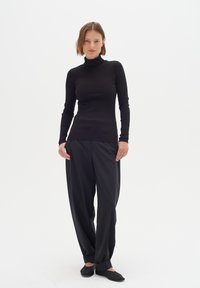 Schwarzes, geripptes Rollkragenoberteil kombiniert mit locker sitzenden schwarzen Hosen. Das Outfit wird mit flachen schwarzen Schuhen ergänzt und betont einen monochromen Look.