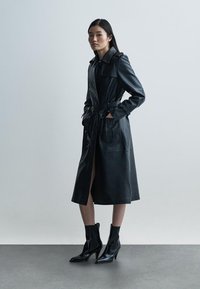 Svart skinntrenchcoat med knäppning framtill, sidofickor och bälte. Har krage och långa ärmar. Bärs med svarta ankleboots.