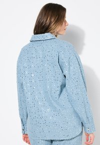 Camicia azzurra con paillettes e colletto, caratterizzata da una vestibilità comoda, maniche lunghe e polsini con bottoni, che presenta una superficie testurizzata e scintillante.