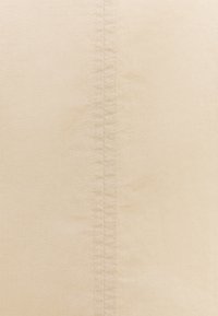 Beige tyg med en slät textur, med en vertikal sömdetalj som går ner i mitten. Inga mönster eller hårdvara synliga.