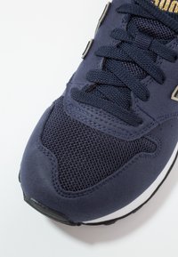 Marinblå sportskor i mesh och mocka, rund tå, platta snörningar och en vit gummisula med svarta detaljer.